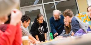 A prof stands at a table surrounded by students as they look at something together.